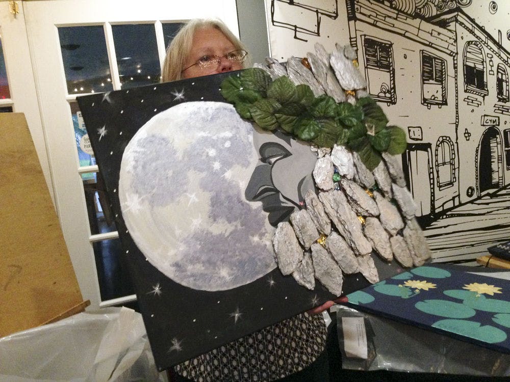 <p class="p1">Event coordinator Maggie Hannon displays “Father Time,” a mixed-media piece by Catherine Kennedy, at the Reframing Recovery artisan exhibit for artists overcoming mental illness Saturday at Cymplify.</p>