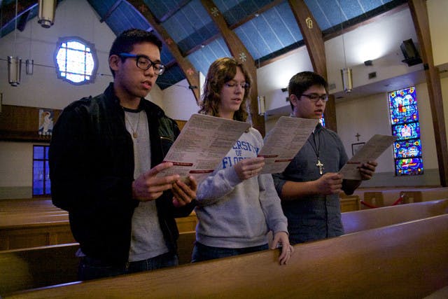 Sherwin Rio, a 19-year-old art and criminology sophomore, and seniors Mary Hart, 23, an aerospace engineering major, and Melnard Rio, 21, a civil engineering major, read pew cards with the new Catholic prayers on them.