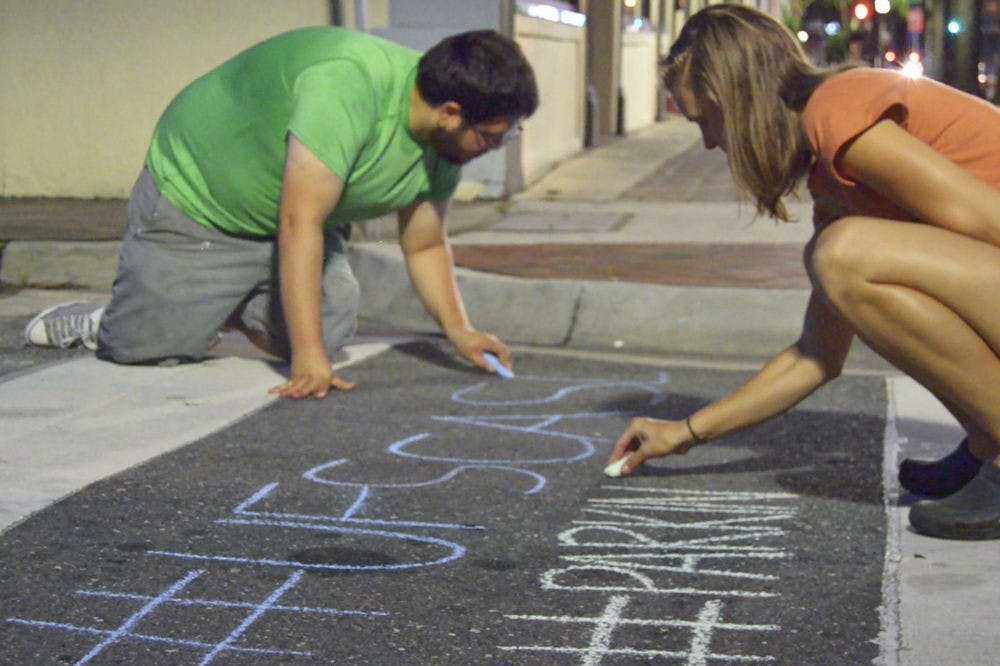 Daniel Rodriguez (left), a UF landscape architecture junior, and Lea Kindt, a UF landscape architecture freshman, both members of UF’s student chapter of America's Society of Landscape Architects chapter, write twitter hashtags on pavement downtown Saturday for the (PARK)ing Day event. The chapter coordinated with the Florida Community Design Center and Pop GNV to create "pop-up parks" on several corners of Northeast First Avenue on Friday and Saturday.