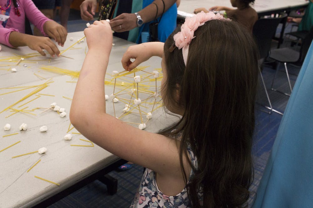 A Girl Scout uses dry spaghetti and mini marshmallows to create different structures.