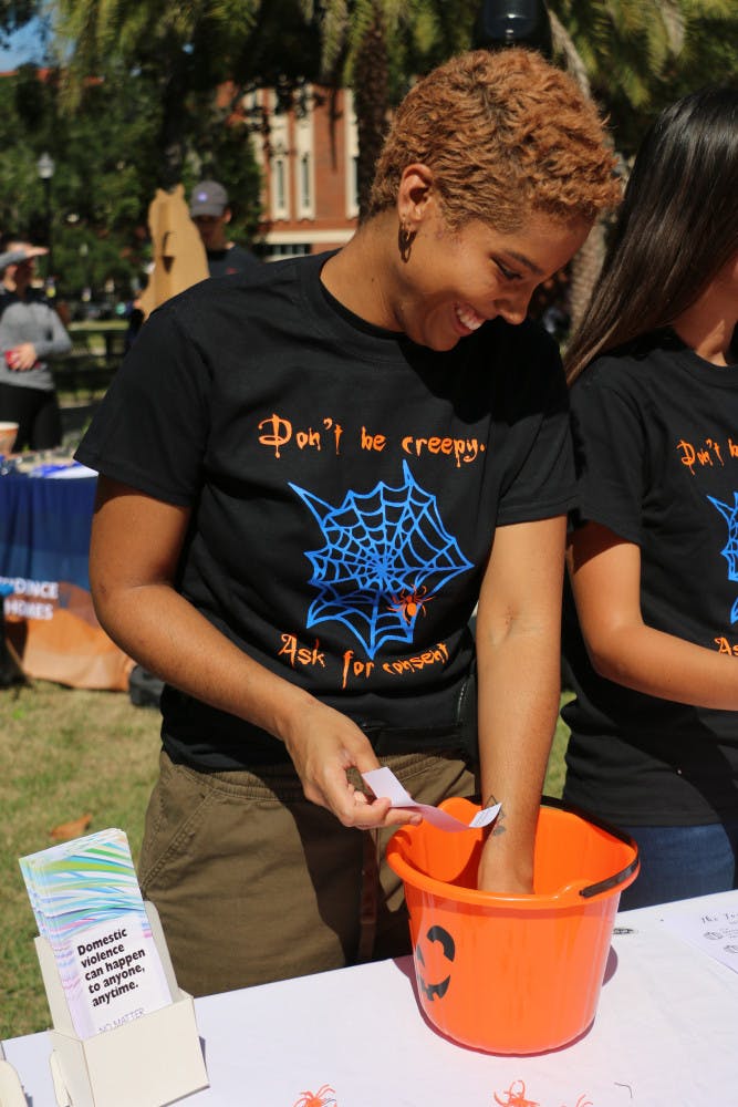 Alissa Adam, a 21-year-old UF women's studies and African-American studies senior, reads off some of the myths and facts of domestic violence during the My Costume is Not Consent tabling event at the Plaza of the Americas Wednesday afternoon. This event was hosted by the UFPD Office of Victim Services. Volunteers like Adam represented 11 other organizations that deal with domestic violence and its effects in the Gainesville area. 