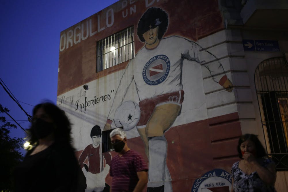 People walk past a mural of Diego Maradona outside the stadium of Argentinos Juniors soccer club, where he started as a professional footballer, in Buenos Aires, Argentina, Wednesday, Nov. 25, 2020. The Argentine soccer great who was among the best players ever and who led his country to the 1986 World Cup title died from a heart attack at his home in Buenos Aires. He was 60.