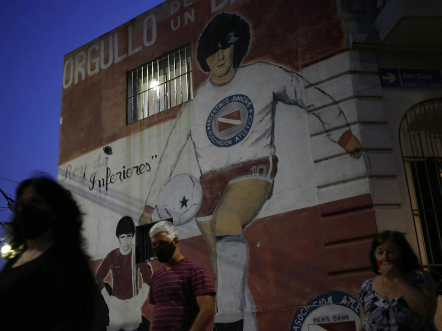 People walk past a mural of Diego Maradona outside the stadium of Argentinos Juniors soccer club, where he started as a professional footballer, in Buenos Aires, Argentina, Wednesday, Nov. 25, 2020. The Argentine soccer great who was among the best players ever and who led his country to the 1986 World Cup title died from a heart attack at his home in Buenos Aires. He was 60.