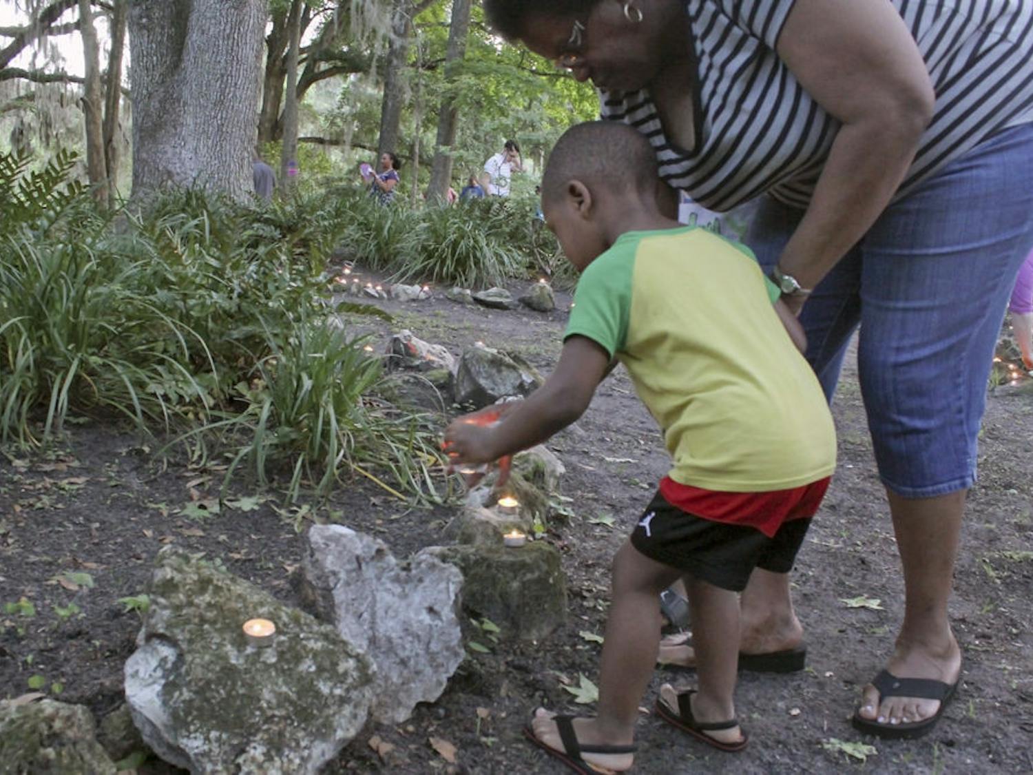 Mykeal Duggan, 3, and grandmother Alice Foreman, 61, place candles at the Victims' Memorial Park in Squirrel Ridge Park on Tuesday. This was the 25th candlelight vigil at the Victims' Memorial Park