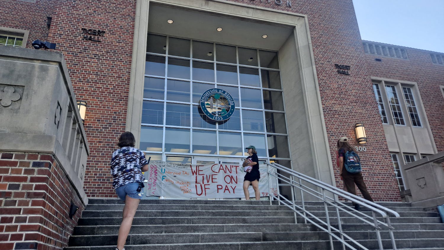 Graduate students gather around a sign reading &quot;we can&#x27;t live on UF pay&quot; at Tigert Hall Friday, June 17, 2022. 