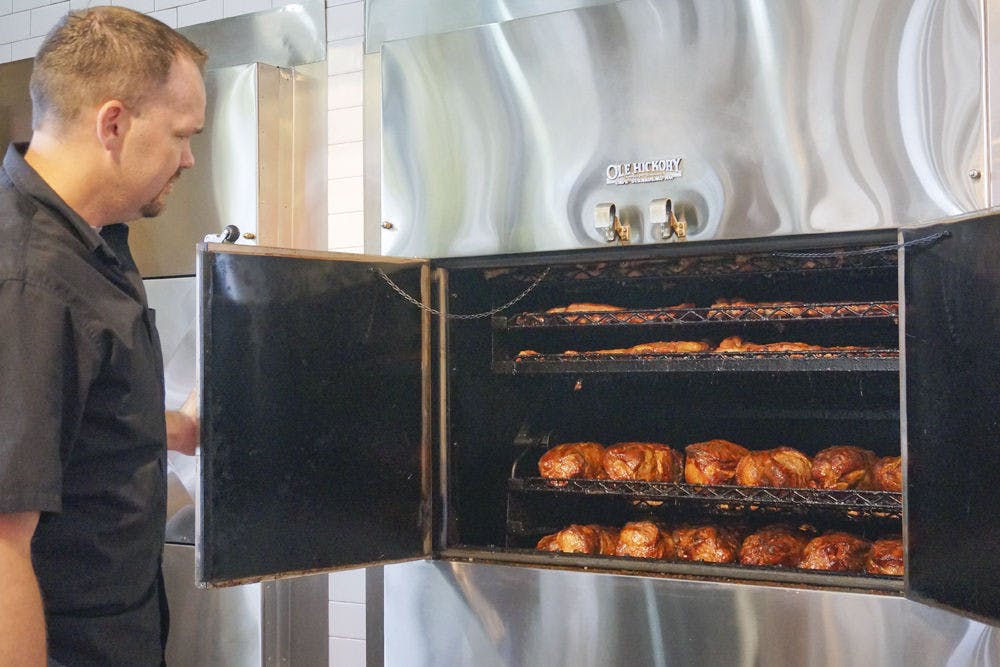 Coy Joyner, assistant general manager, opens one of the barbecue smokers at Sonny’s BBQ on 3635 SW Archer Road. The restaurant’s new building emphasizes the oak wood smokers, putting them in full view of guests.