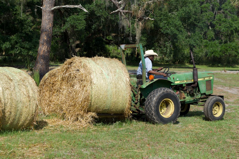 Farmer John Nix moves a bale of hay with a tractor near his cow pasture on Saturday, April 15, 2023.