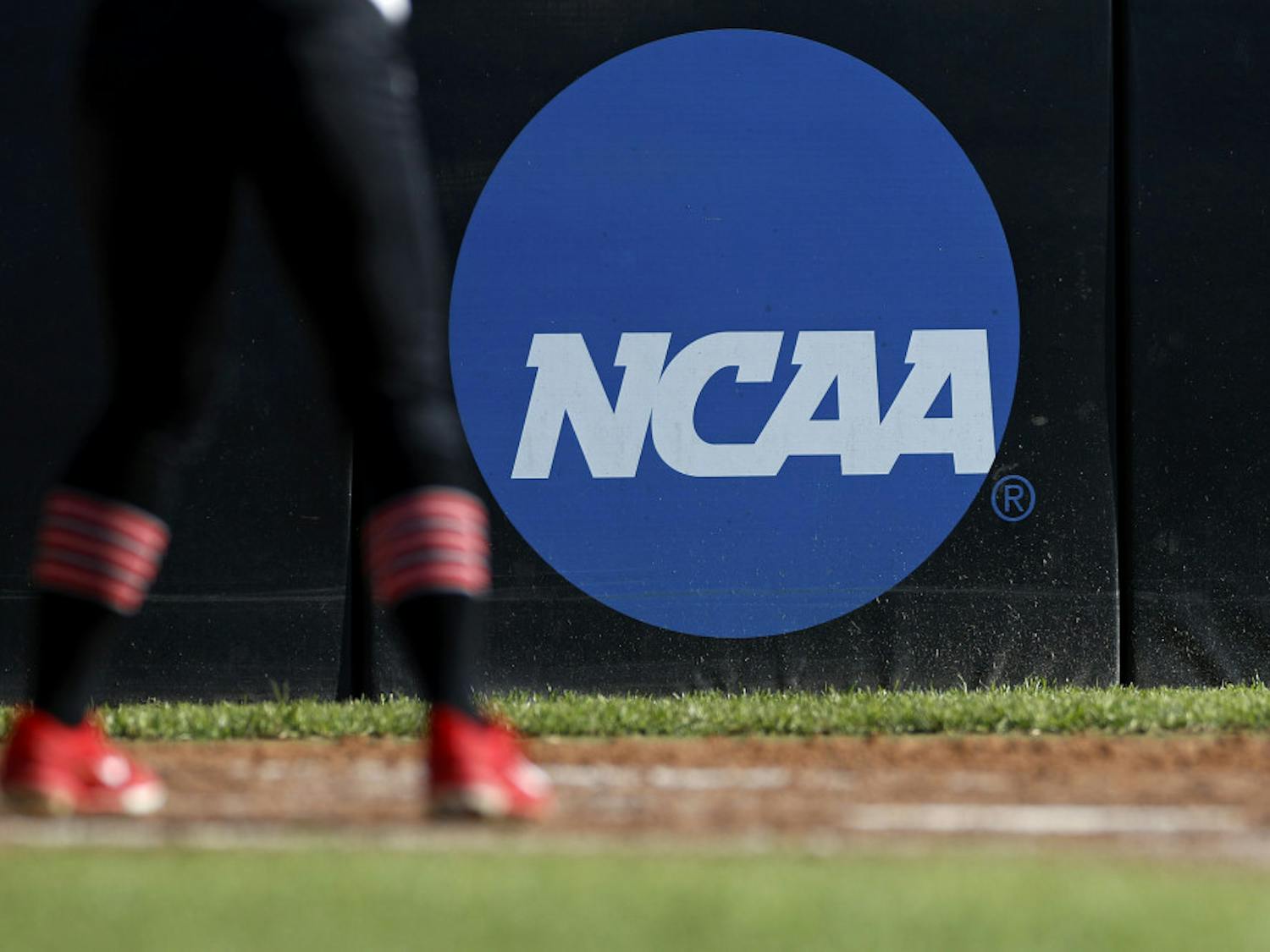 FILE - In this April 19, 2019, file photo, an athlete stands near a NCAA logo during a softball game in Beaumont, Texas. The NCAA is poised to take a significant step toward allowing college athletes to earn money without violating amateurism rules. The Board of Governors will be briefed Tuesday, Oct. 29 by administrators who have been examining whether it would be feasible to allow college athletes to profit of their names, images and likenesses. A California law set to take effect in 2023 would make it illegal for NCAA schools in the state to prevent athletes from signing personal endorsement deals. (AP Photo/Aaron M. Sprecher, File)