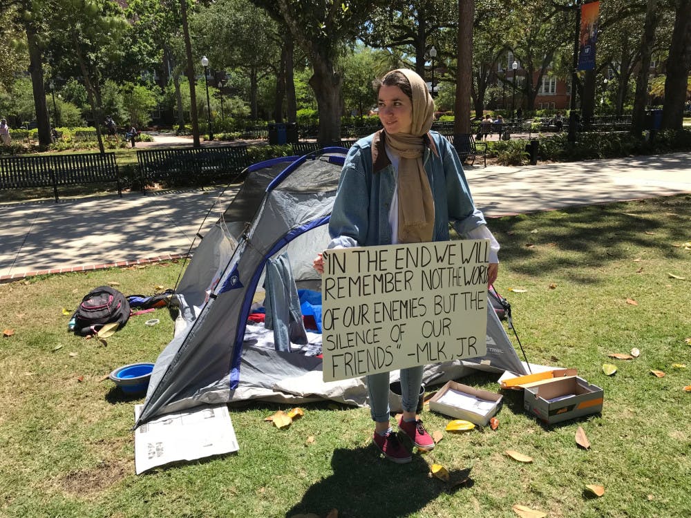 <p>Sophia Timm, a 21-year-old UF biology and anthropology senior and the Students Organize for Syria’s chair for the Books Not Bombs campaign, holds up a sign outside the mock-refugee tent. Students Organize for Syria say the display simulates the living conditions of refugees fleeing the Syrian Civil War.</p>