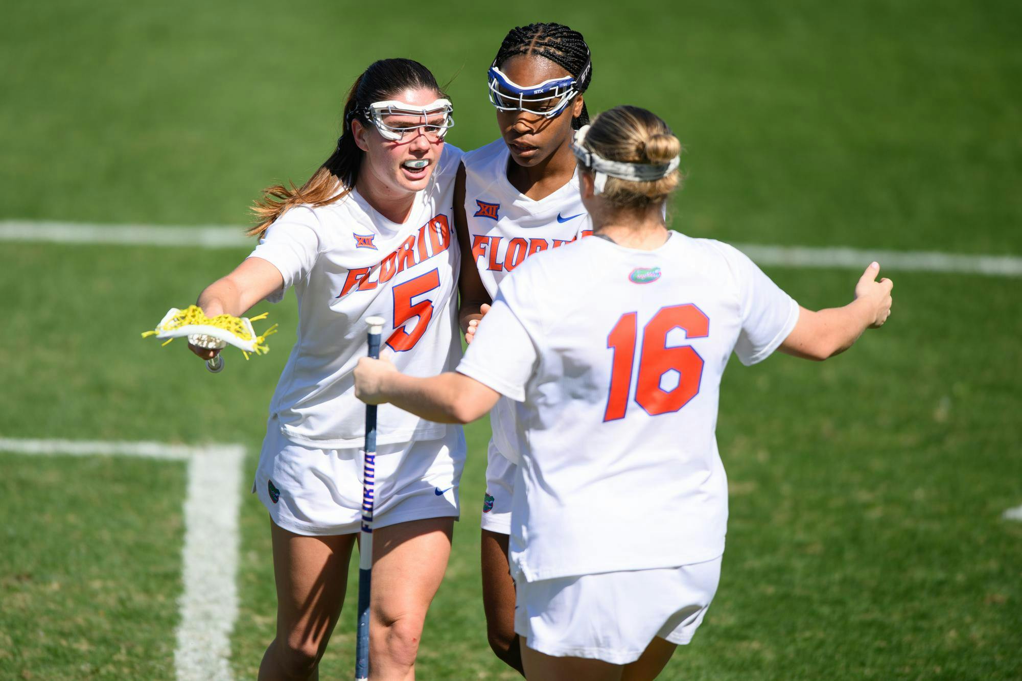 Florida midfielder Kaitlyn Davies (5) embraces attacker Clark Hamilton (21) and attacker Frannie Hahn (16) after scoring a goal during the second half of an NCAA lacrosse match against Michigan, Friday, Feb. 13, 2026, in Gainesville, Fla.