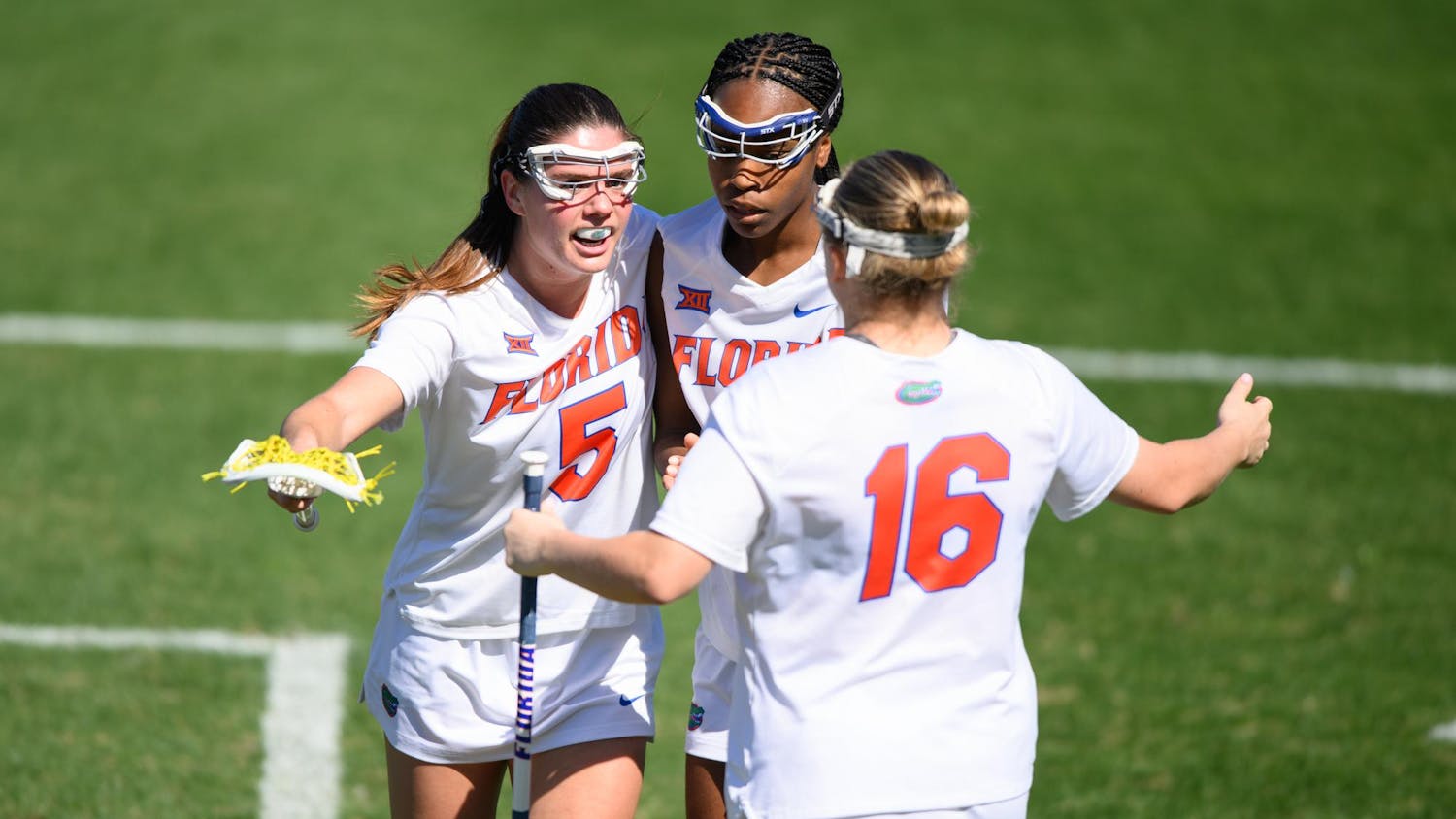 Florida midfielder Kaitlyn Davies (5) embraces attacker Clark Hamilton (21) and attacker Frannie Hahn (16) after scoring a goal during the second half of an NCAA lacrosse match against Michigan, Friday, Feb. 13, 2026, in Gainesville, Fla.