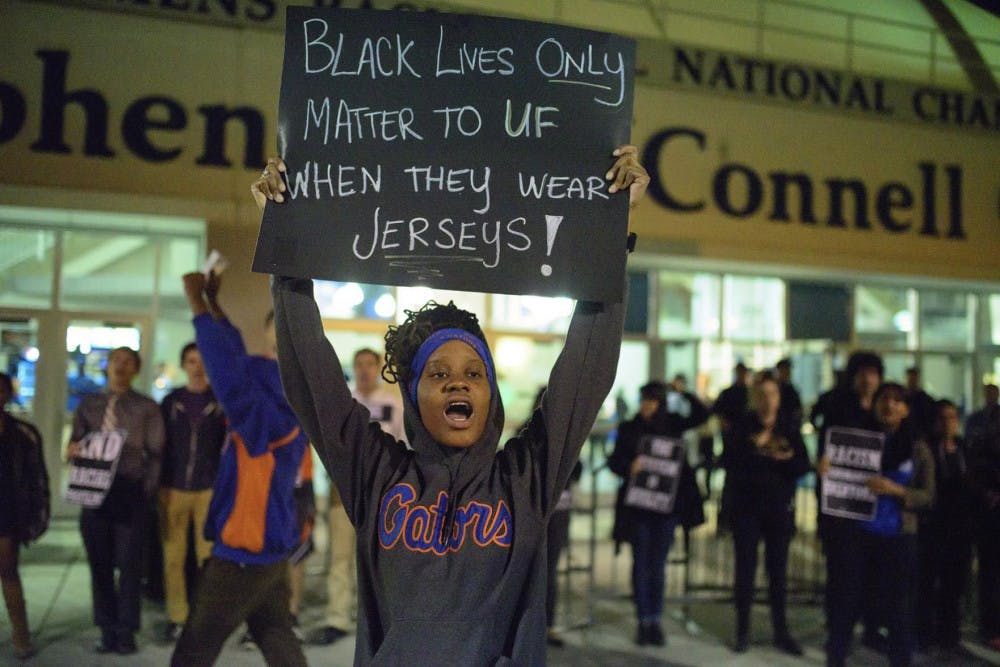 A protester outside the Stephen C. O’Connell center holds a sign with a statement implying the University of Florida is only concerned with African-Americans that participate in athletics at the school.