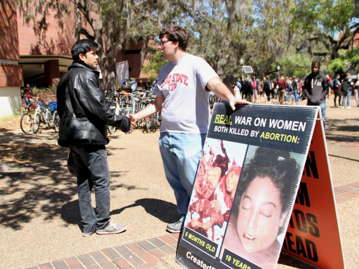 Alfredo Patiño, 22, a UF senior political science and sociology major, and Joe Trammel, 22, a law student from Ohio State University and member of the Created Equal organization, shake hands. Patiño and Trammel had a respectful conversation about the images the Created Equal organization placed on Turlington Plaza on Tuesday.