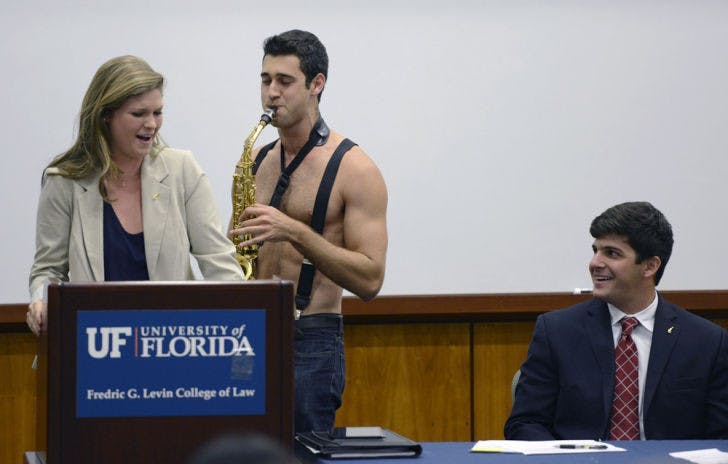 David Greenstein plays saxophone shirtless to Senate President Lauren Verno as Senate President Pro Tempore Cory Yeffet laughs Tuesday evening during the weekly Student Senate meeting at the Levin College of Law. Greenstein’s performance was part of a video promo for the 2013 Gator Growl.