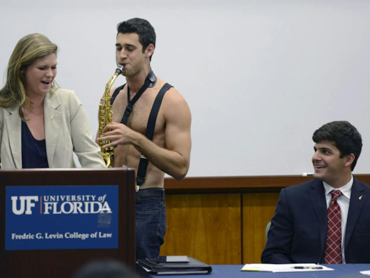 David Greenstein plays saxophone shirtless to Senate President Lauren Verno as Senate President Pro Tempore Cory Yeffet laughs Tuesday evening during the weekly Student Senate meeting at the Levin College of Law. Greenstein’s performance was part of a video promo for the 2013 Gator Growl.