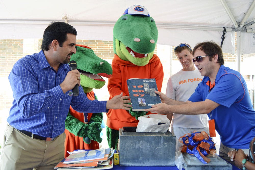 Tony Medina (left), president of the UF Association of Hispanic Alumni, announces Saturday morning the contents of a time capsule buried in 1996 by the UF Class of 1995. Bruce Floyd (far right), social media manager for the University of Florida Athletic Association and member of the Class of 1995, holds a copy of the 1996-1997 undergraduate catalogue, while Dan Clarke, 43, also a member of the Class of 1995, looks on.
