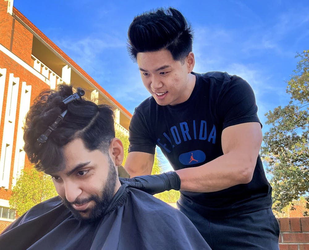 Shahmir Memon, a 21-year-old business administration junior, receives a fresh cut on the Plaza of the Americas lawn on Friday, Jan. 14. From bathroom stalls to street corners, Ju-Ray Kuo, a 24-year-old applied physiology and kinesiology master's student at UF, has been giving free cuts throughout Gainesville for the past six years.