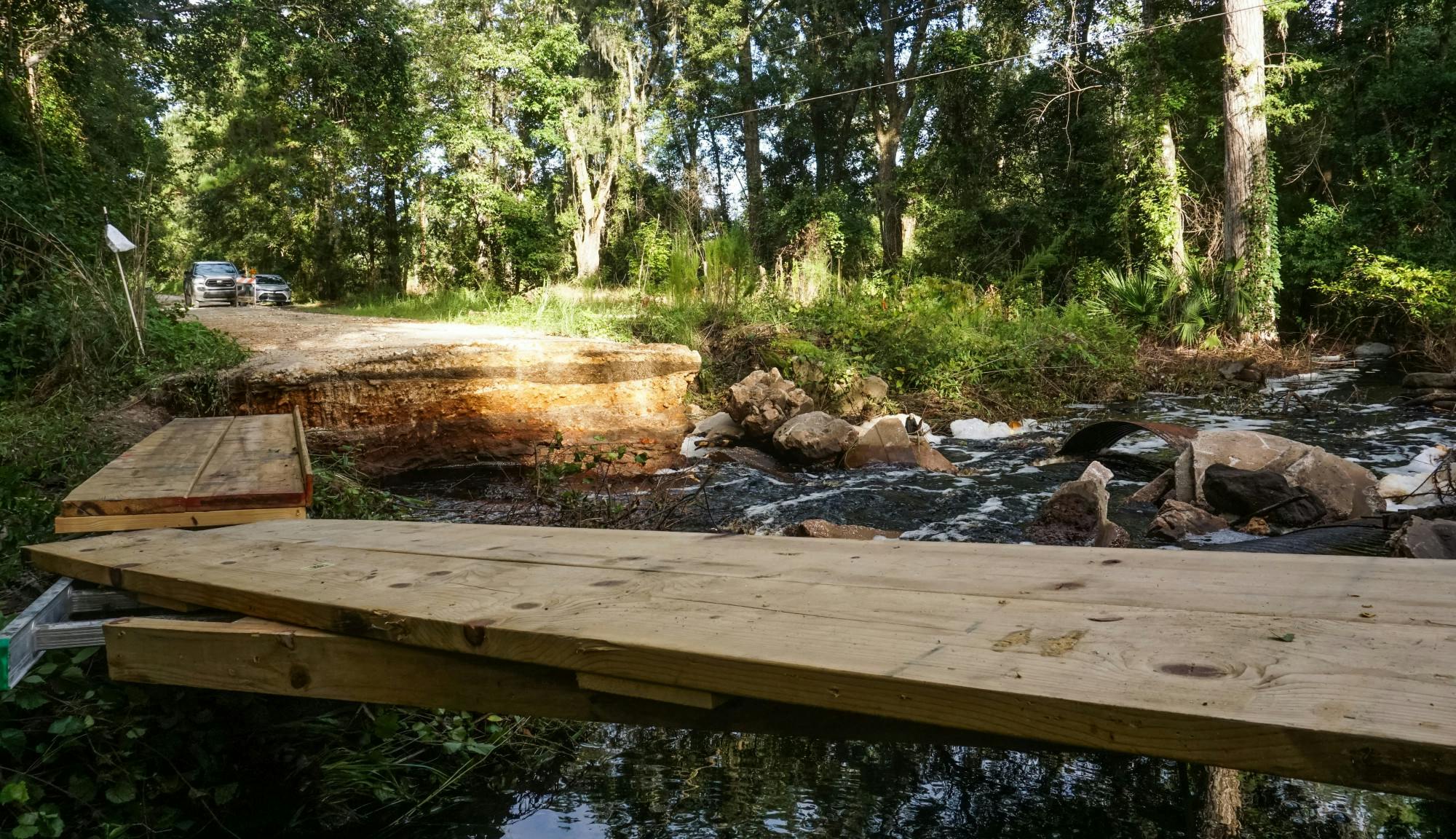 Water rushes under the collapsed part of Northeast 100th Avenue on Saturday, July 10, 2021. The small bridge’s culverts couldn’t handle the fast-flowing storm water runoff produced by Tropical Storm Elsa.