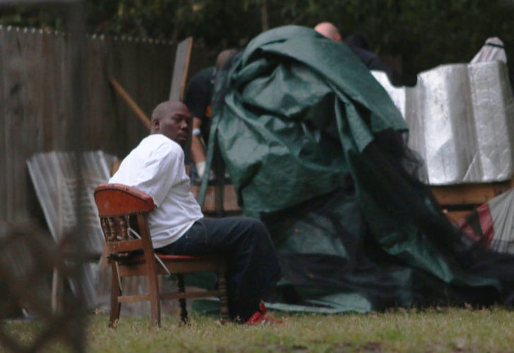 <p>An unidentified detainee sits outside one of the four properties authorities were investigating Wednesday evening. Officers simultaneously executed four search warrants on Northeast Third Avenue and Northeast Third Place as part of a narcotics investigation.</p>