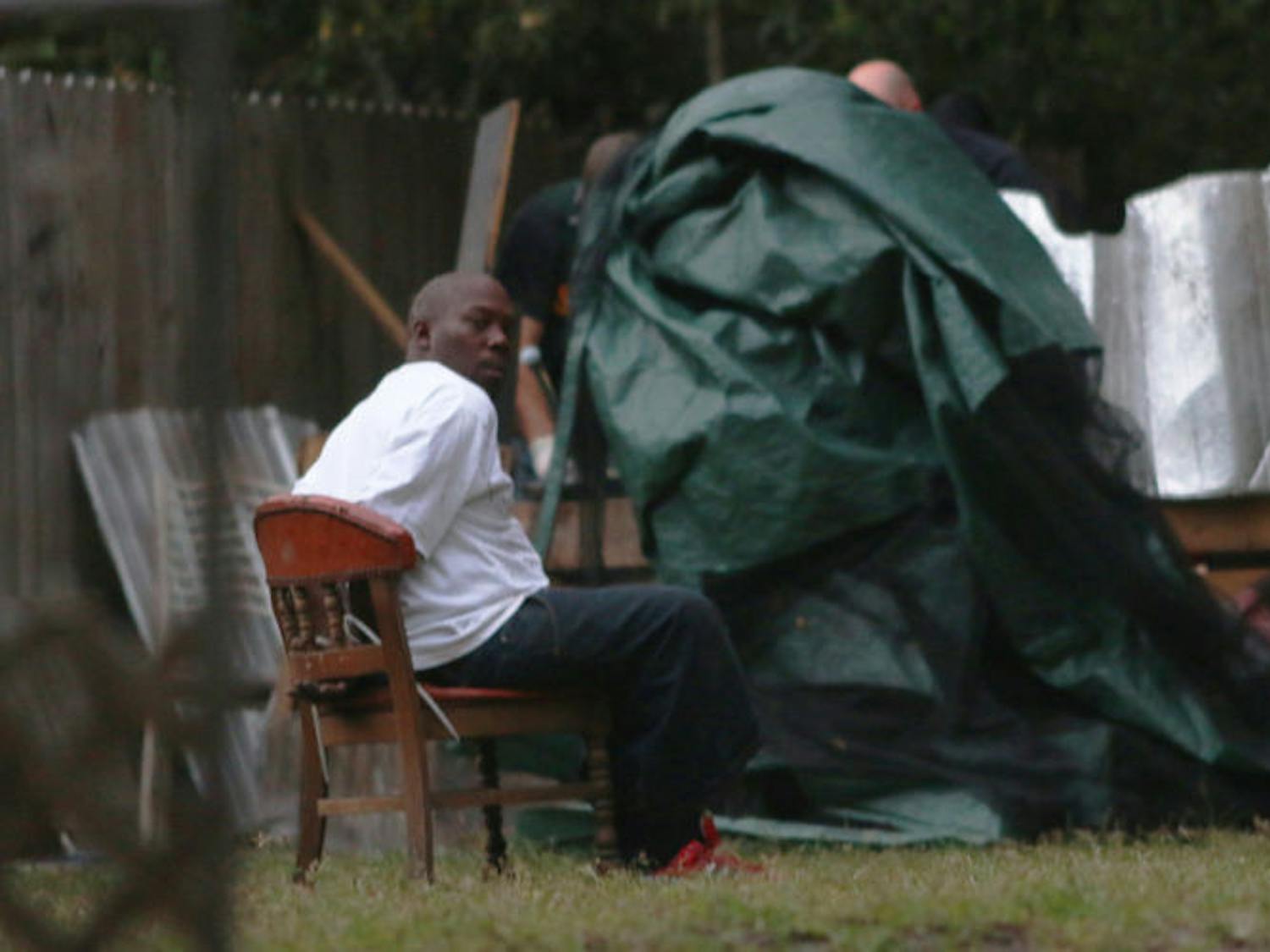An unidentified detainee sits outside one of the four properties authorities were investigating Wednesday evening. Officers simultaneously executed four search warrants on Northeast Third Avenue and Northeast Third Place as part of a narcotics investigation.