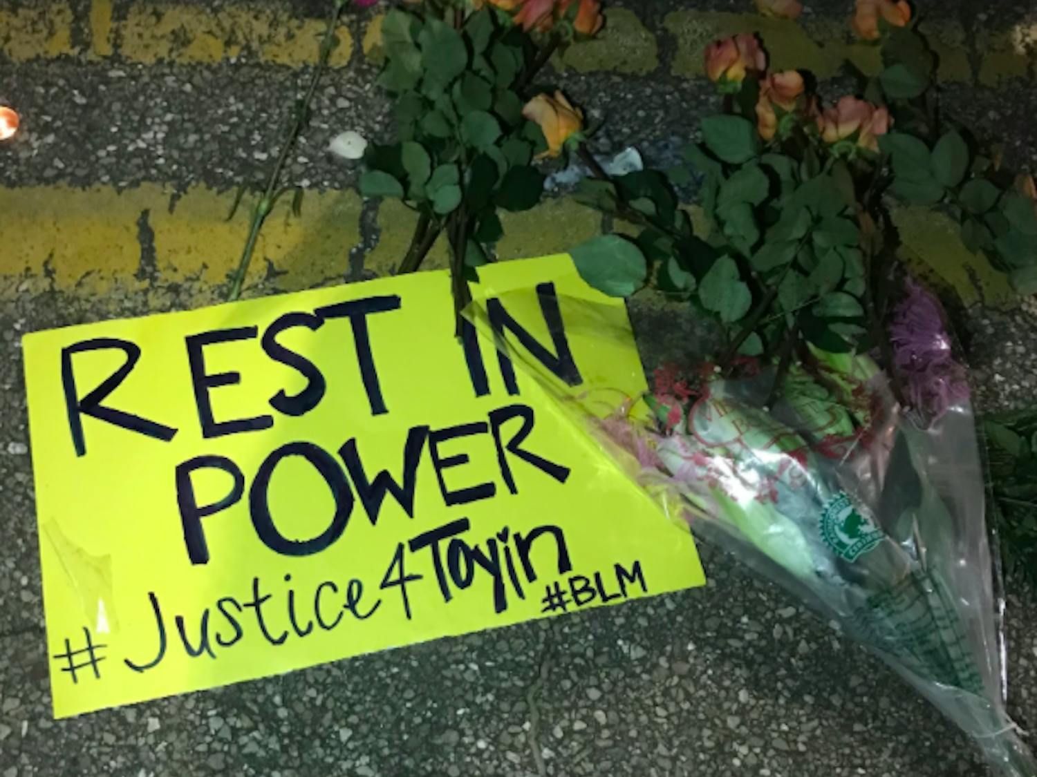 A poster that reads “REST IN POWER” and “#Justice4Toyin #BLM” lays on Monday Road in Tallahassee next to a row of flowers and candles.