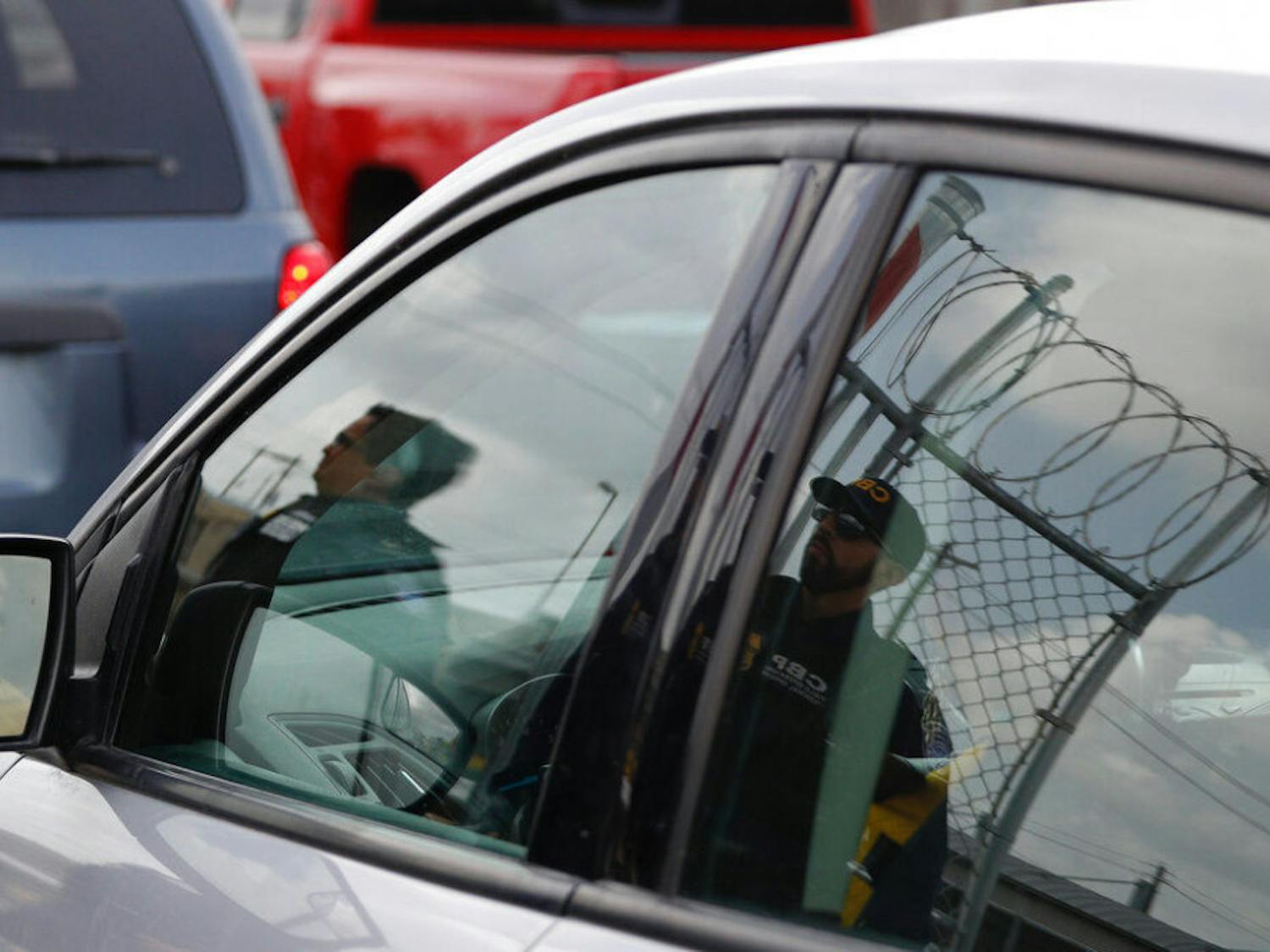 Customs and Border Protection agents are reflected in the window of an entering car, as they survey vehicles entering the U.S. on the Puerta Mexico international bridge leading into Brownsville, Texas from Matamoros, Mexico, Friday, June 28, 2019. Hundreds of migrants from Central America, South America, the Caribbean and Africa have been waiting for their number to be called at the bridge in downtown Matamoros, to have the opportunity to request asylum in the U.S.