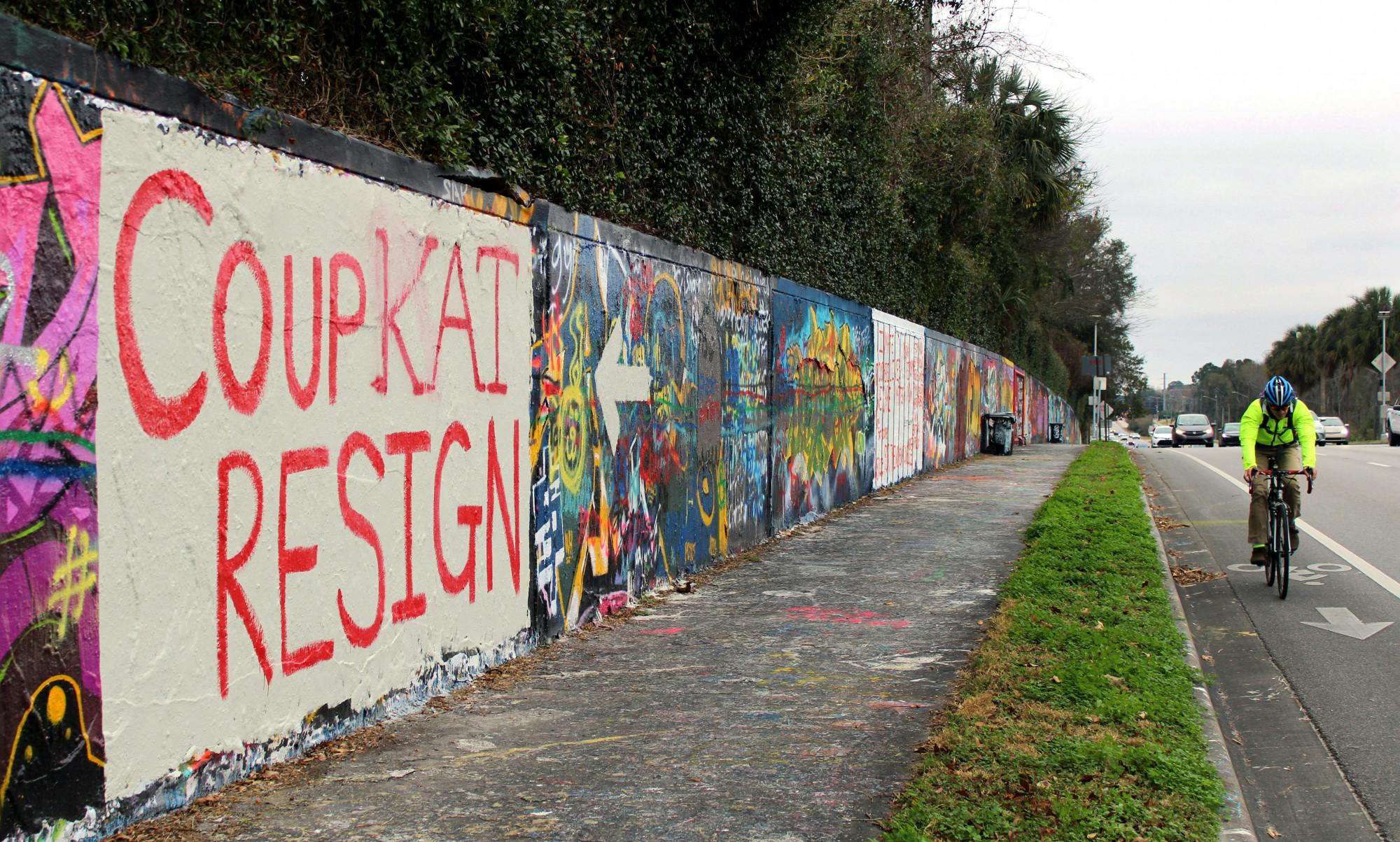 A cyclist and cars pass by a mural on a wall along Northwest 34th Street that reads "Coup Kat Resign" in Gainesville, Tuesday, Jan. 12, 2021. The mural refers to the newly elected U.S Representative Kat Cammack.