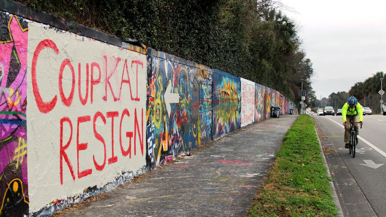 A cyclist and cars pass by a mural on a wall along Northwest 34th Street that reads "Coup Kat Resign" in Gainesville, Tuesday, Jan. 12, 2021. The mural refers to the newly elected U.S Representative Kat Cammack.