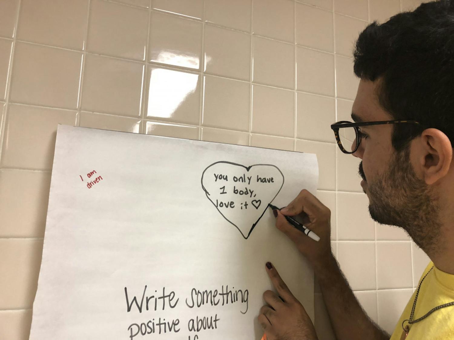 Anthony Flores, a 20-year-old UF visual art studies sophomore, traces a heart around a message they wrote.   