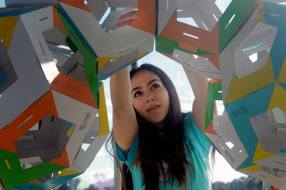 Stephany Larez, a 19-year-old freshman health science major at Santa Fe College, volunteers Saturday morning at the Collective Paper Aesthetics exhibit. She enjoys working with kids at the exhibit and loves “the whole idea of mixing science and art together.”&nbsp;The gallery allowed visitors to build with foldable dye cut pieces in order to eventually create a larger structure from thousands of the smaller pieces, said Ellie Thom, the senior manager of Exhibit and Visionaries at the Cade Museum.&nbsp;