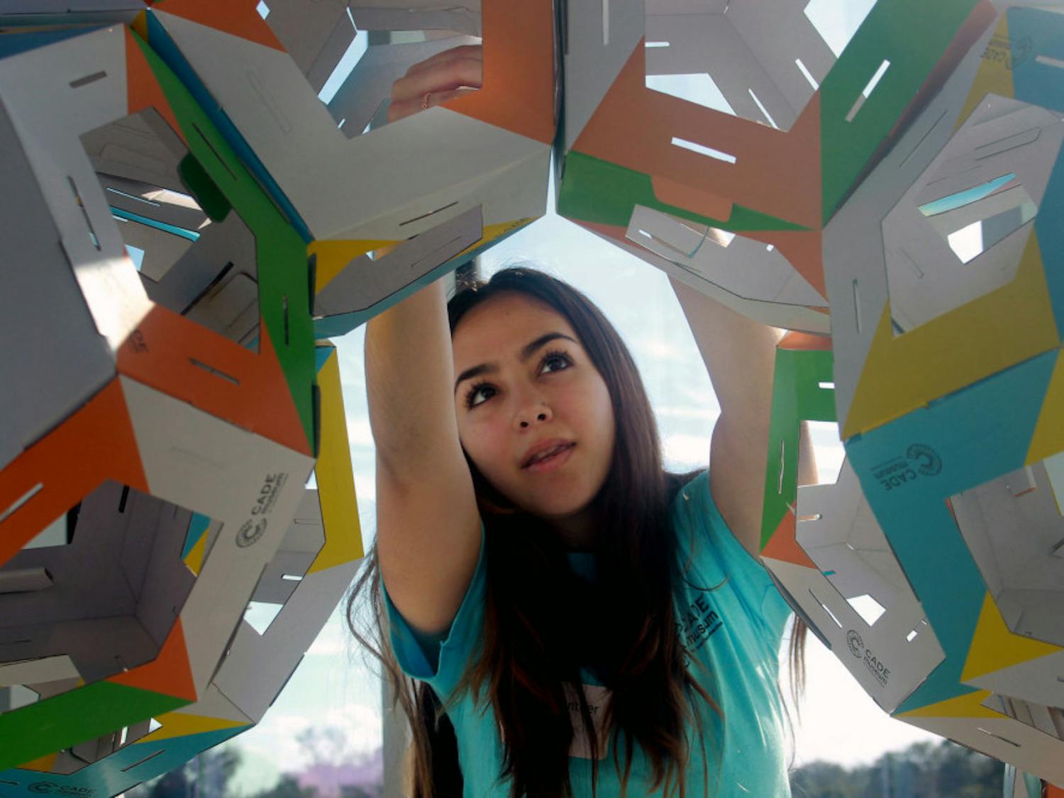 Stephany Larez, a 19-year-old freshman health science major at Santa Fe College, volunteers Saturday morning at the Collective Paper Aesthetics exhibit. She enjoys working with kids at the exhibit and loves “the whole idea of mixing science and art together.” The gallery allowed visitors to build with foldable dye cut pieces in order to eventually create a larger structure from thousands of the smaller pieces, said Ellie Thom, the senior manager of Exhibit and Visionaries at the Cade Museum. 
