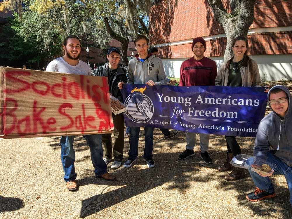 <p><span id="docs-internal-guid-84167e4d-d4f9-954e-6afe-a641616aa8a6"><span>Members of UF’s Young Americans for Freedom pose in front of a sign advertising their socialist bake sale on Turlington Plaza on Wednesday. Members of the student organization sold cookies and doughnuts, giving some away, to point out the issues with socialism.</span></span></p>