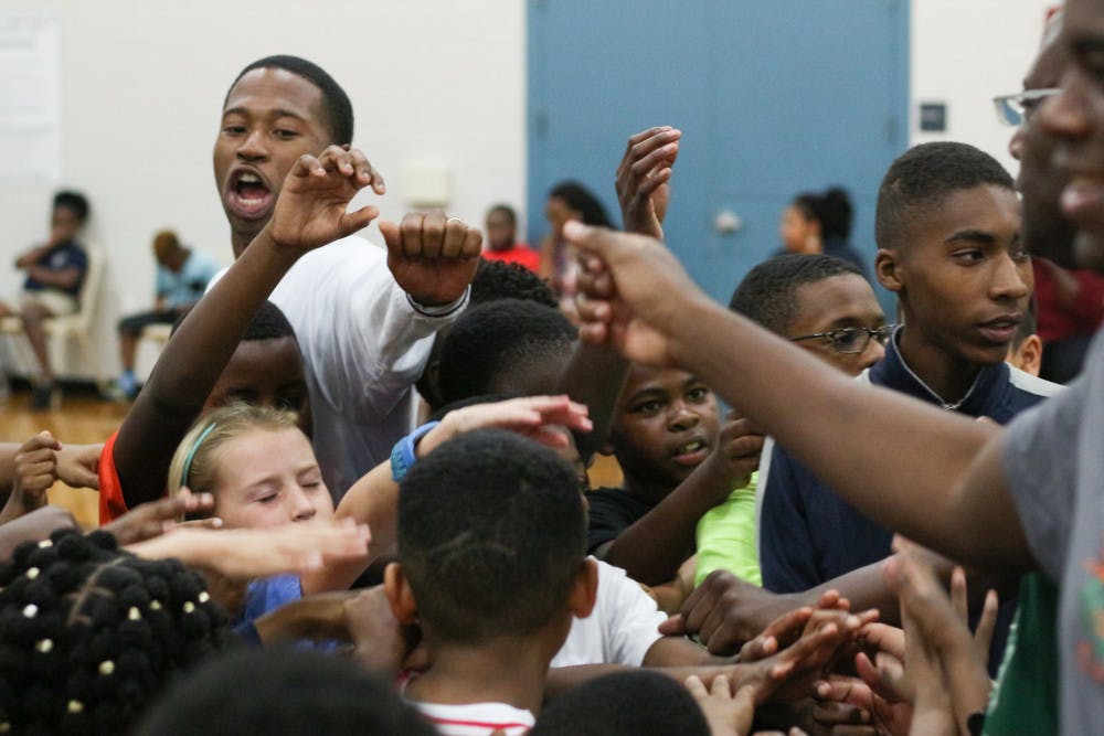 <p>From left: Ron Larris, a 30-year-old trainer at Nigie Hoops and former Gainesville High School basketball player, cheers “Team!” with 46 kids and some Eastside High School basketball coaches during a free basketball clinic held at the Martin Luther King Jr. Multipurpose Center on Monday night.</p>
