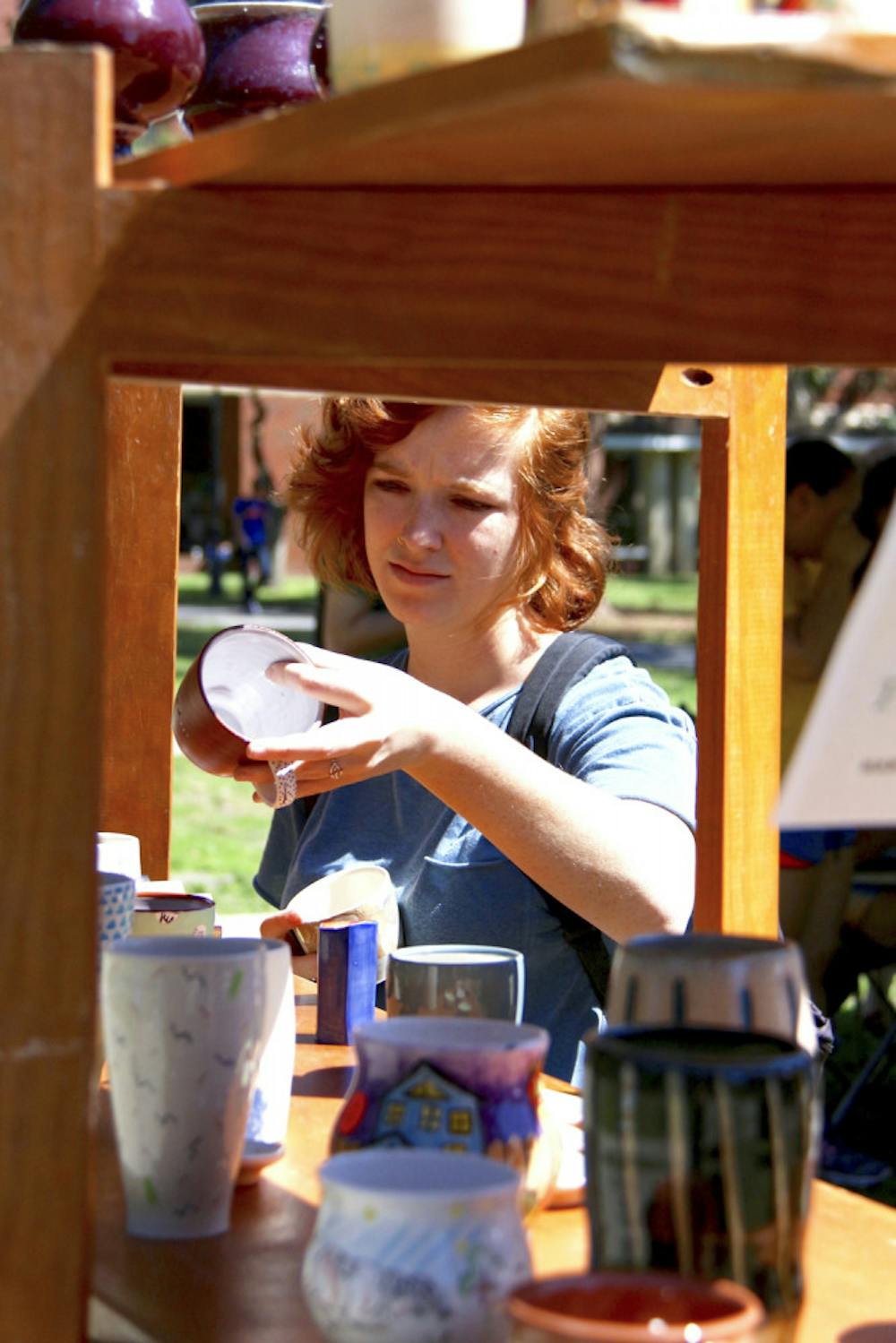 <p>Erin Wagner, 21, examines ceramic cups on the Plaza of the Americas at the Handbuilt or Thrown Clay Spring Sale on Monday. The UF art junior said she admired the work of Stephanie Wilhelm, who she said worked with bodies a lot.</p>