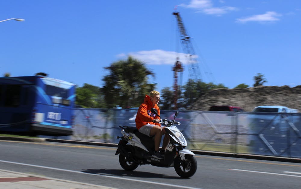 A person wearing a UF sweatshirt rides past a construction site on Museum Road across from the Reitz Union on Friday, March 19, 2021. (Photo by Chasity Maynard)