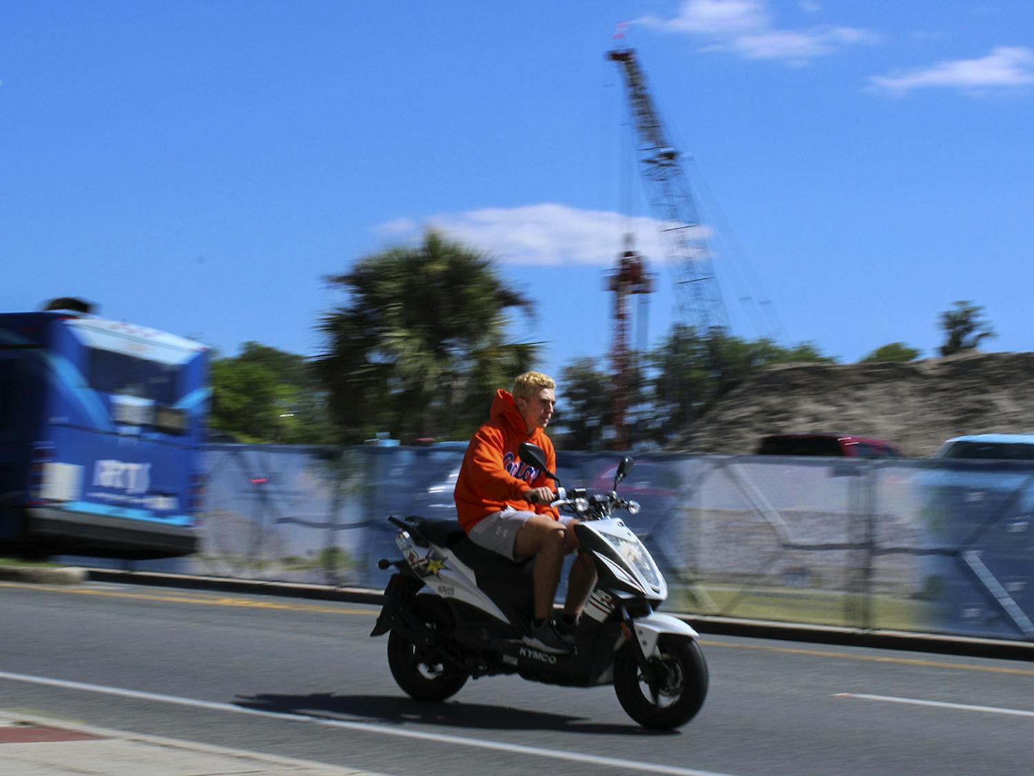 A person wearing a UF sweatshirt rides past a construction site on Museum Road across from the Reitz Union on Friday, March 19, 2021. (Photo by Chasity Maynard)