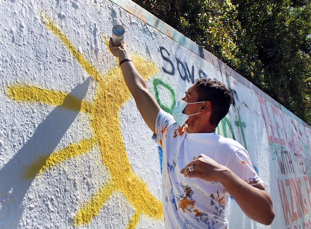 Oscar Santiago, 18, a political science freshman, finishes spray painting a sun on a mural that reads "Save our Bright Futures" on Sunday, March 7, 2021. The mural was painted in response to Senate Bill 86, which would limit some students’ access to state funding, including the Bright Futures scholarship.