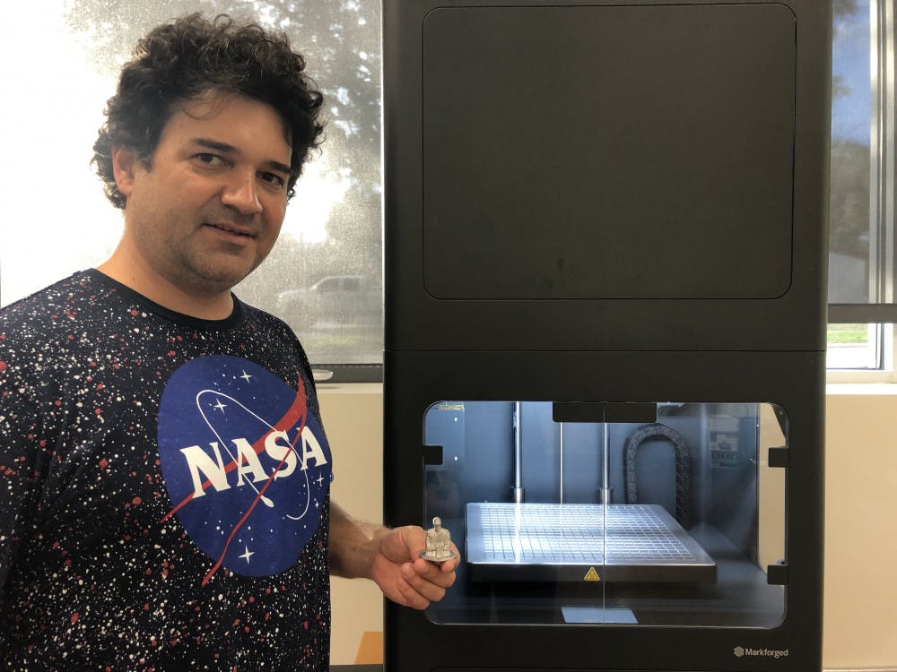 Juan Griego stands next to the 3D metal printer with a model he printed of race car driver Dale Earnhardt, one of the first pieces made by the new printer. The replica is based off a miniature he used for an art project. Kelly Hayes / Alligator Staff