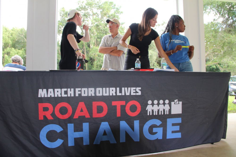 Tom Bergan, David Finley, Ingrid Fernandes and Gracey Jean-Bernard stand behind a booth for “March for our Lives — Road to Change.”