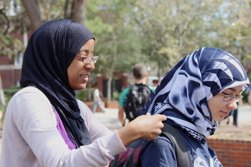 <p>Heiba Belal, 21, left, a UF microbiology senior, helps Lisdelys Garcia, 19, a UF biomedical engineering freshman, put on her hijab, a veil that covers the head, on Turlington Plaza on Monday for Islam on Campus’ “Hijab for a Day.”</p>