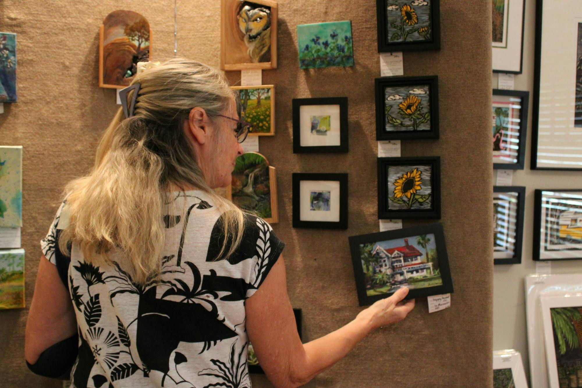 Trude Spillane, a jeweler and painter at the Artisans’ Guild Gallery, tweaks the “Small Works” exhibit, Tuesday, August 18, 2026, in Gainesville, Fla.