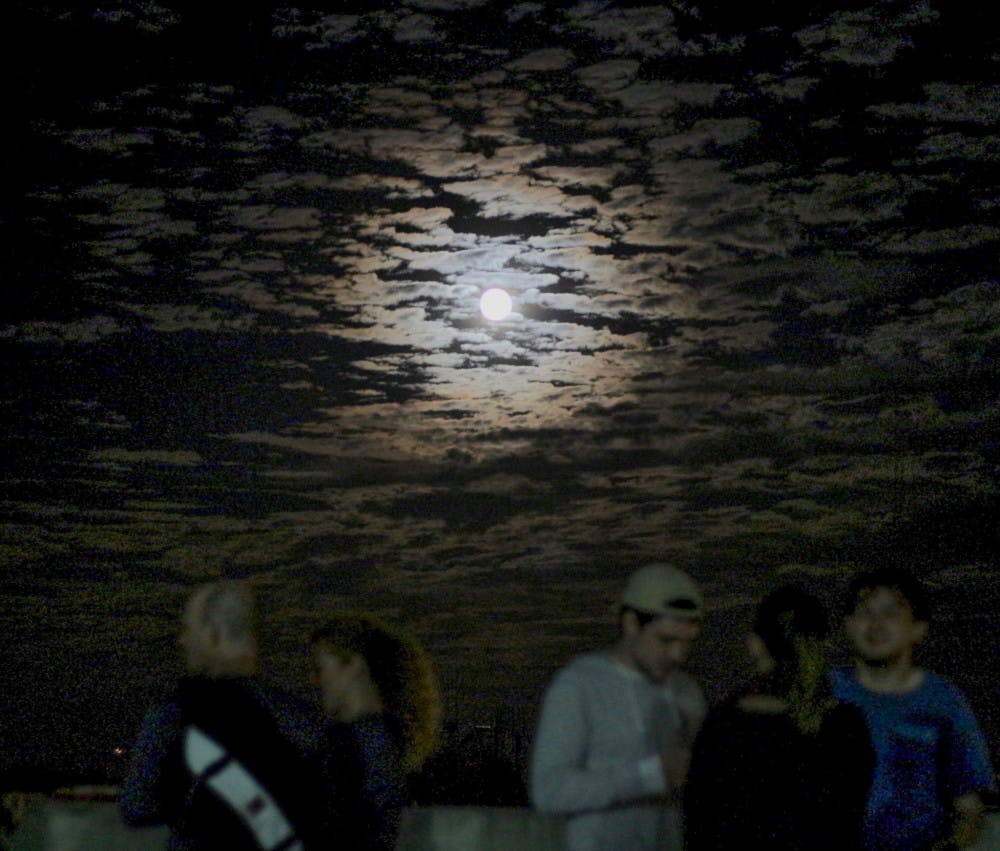 Gainesville residents and UF students watch the supermoon on the roof of a parking garage above Volta Coffee, Tea and Chocolate on Monday night. About 150 people showed up with dogs, roller blades and cameras to see the moon at its brightest and closest location to the Earth until the next supermoon in 2034.