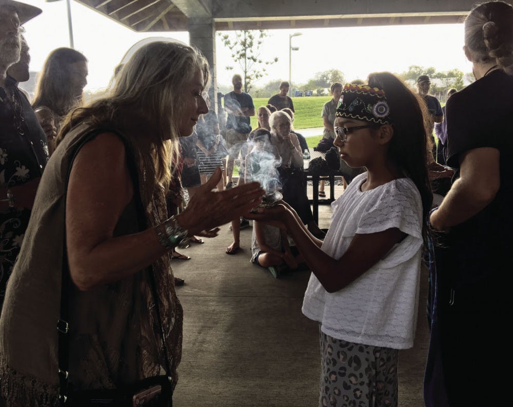 Lily Smith, 11, welcomed guests at a Wednesday night water ceremony held at Depot Park, located at 200 SE Depot Ave., by smudging them with sage. At the ceremony, about 30 people sang, danced and discussed the importance of the four elements — especially water.