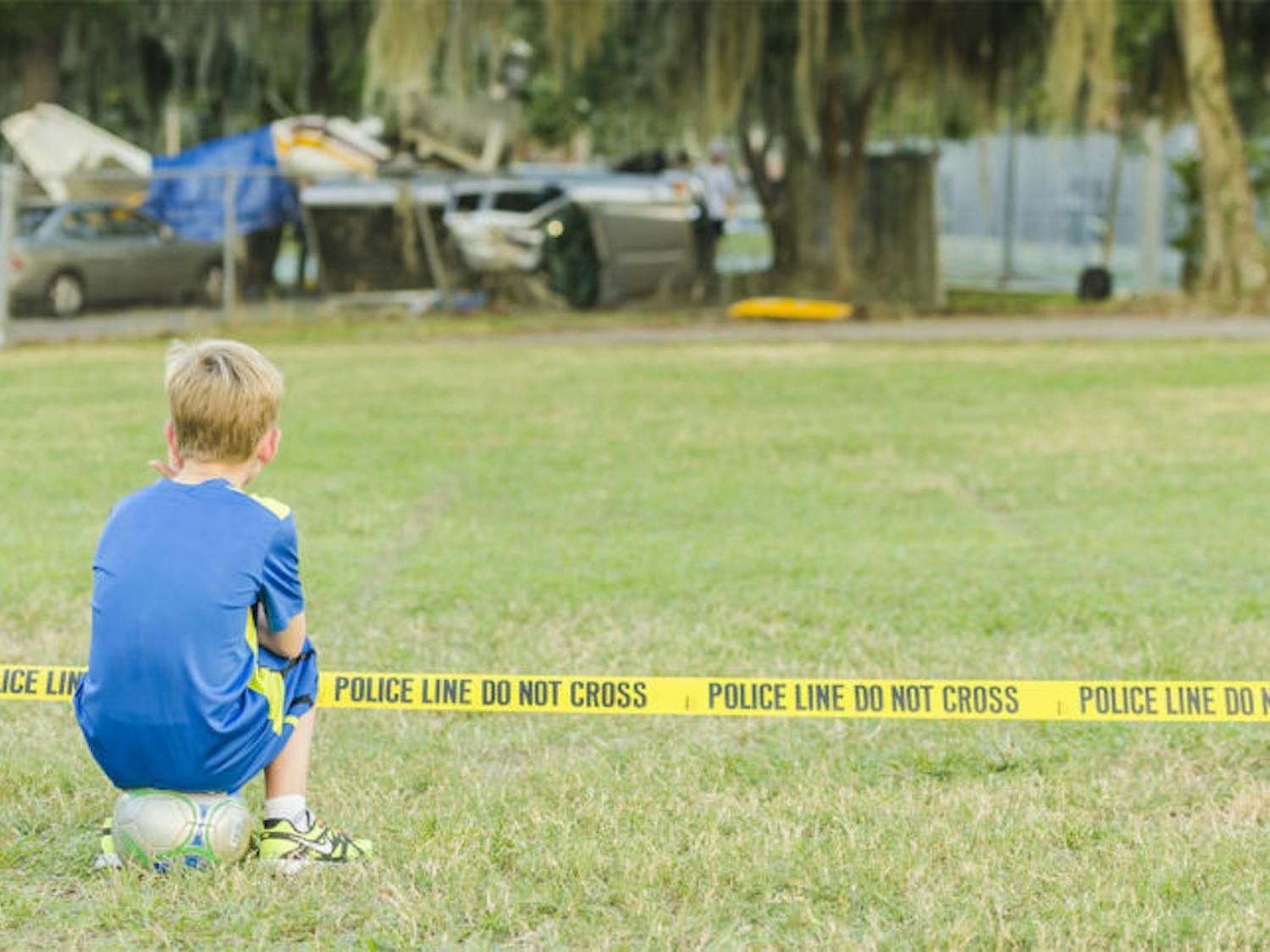 A boy sits behind the police line on Flavet Field on Saturday.