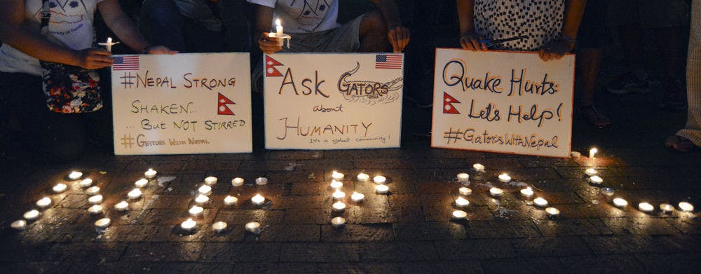 <p>Vigil participants hold signs over a candle letters reading "Nepal."</p>