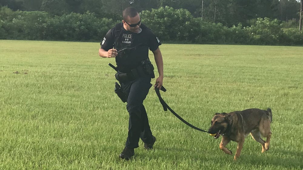 Officer Ed Ratliff and his dog, Ace, run off the field after doing apprehension training. Another officer wore a sleeve for Ace to safely bite down on his forearm.