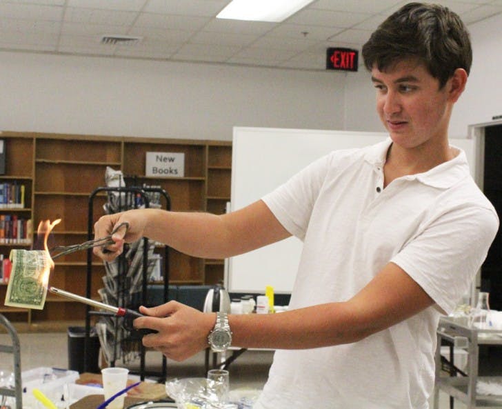 Matthew Bill, an 18-year-old freshman, lights an alcohol-soaked dollar on fire at the potions table during an exhibit at the Health Science Center Library on Thursday.