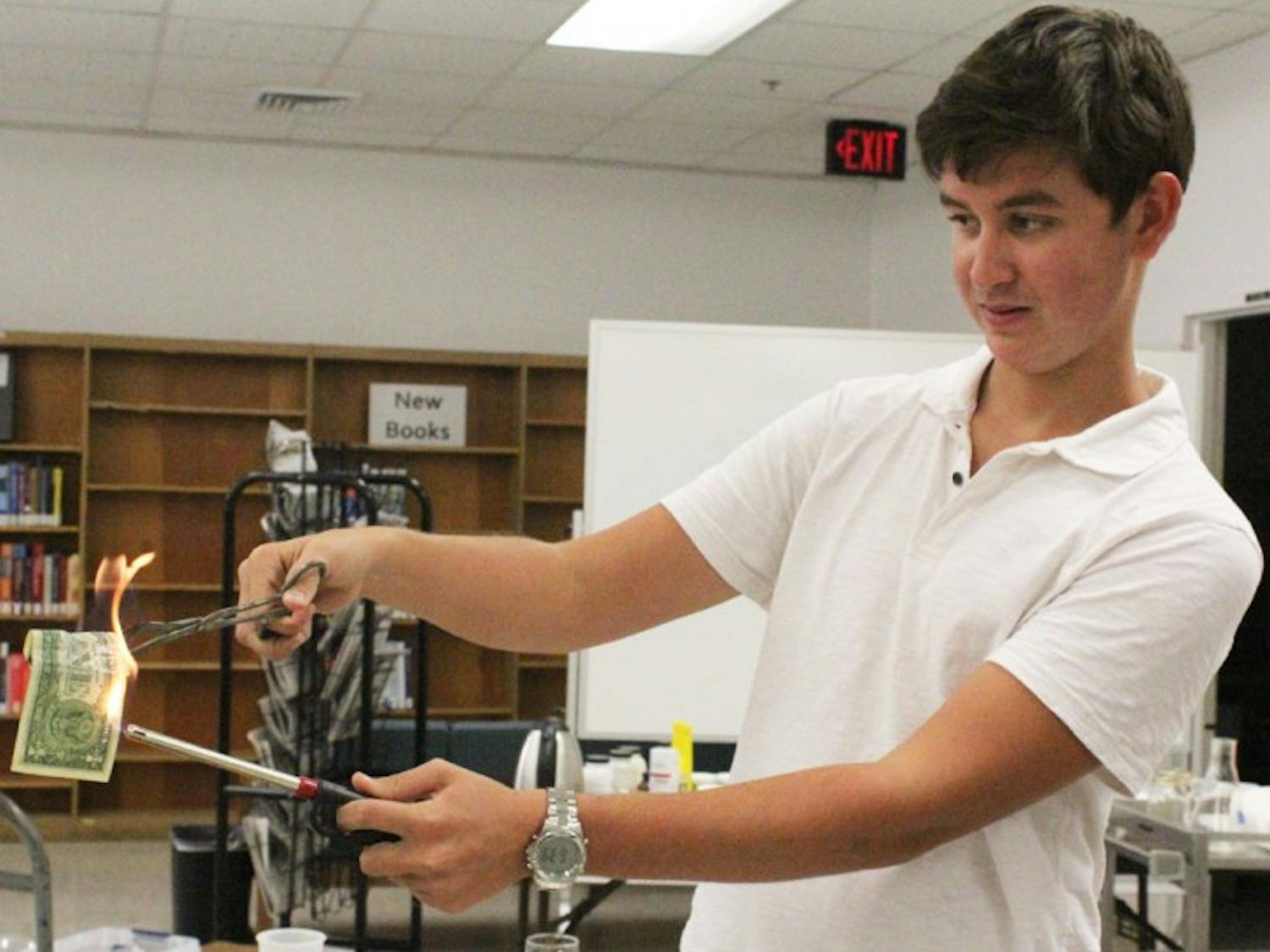 Matthew Bill, an 18-year-old freshman, lights an alcohol-soaked dollar on fire at the potions table during an exhibit at the Health Science Center Library on Thursday.
