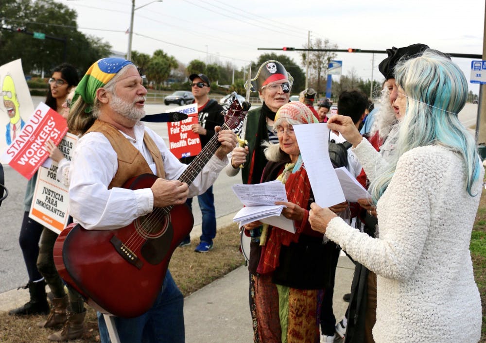 <p>Lee Malis, 58, strums his guitar and sings along with other protesters during the Rep. Ted Yoho Pirate Protest on Friday. Malis wrote a pirate-themed song specifically for the protest which he sang with the protesters around him.</p>