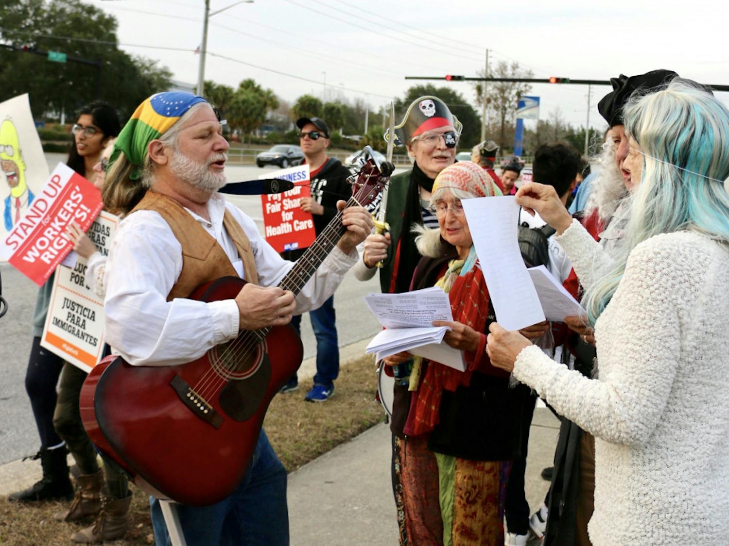 Lee Malis, 58, strums his guitar and sings along with other protesters during the Rep. Ted Yoho Pirate Protest on Friday. Malis wrote a pirate-themed song specifically for the protest which he sang with the protesters around him.